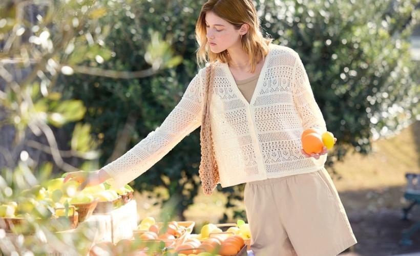 Woman in a knit cardigan picking citrus fruit at an outdoor market