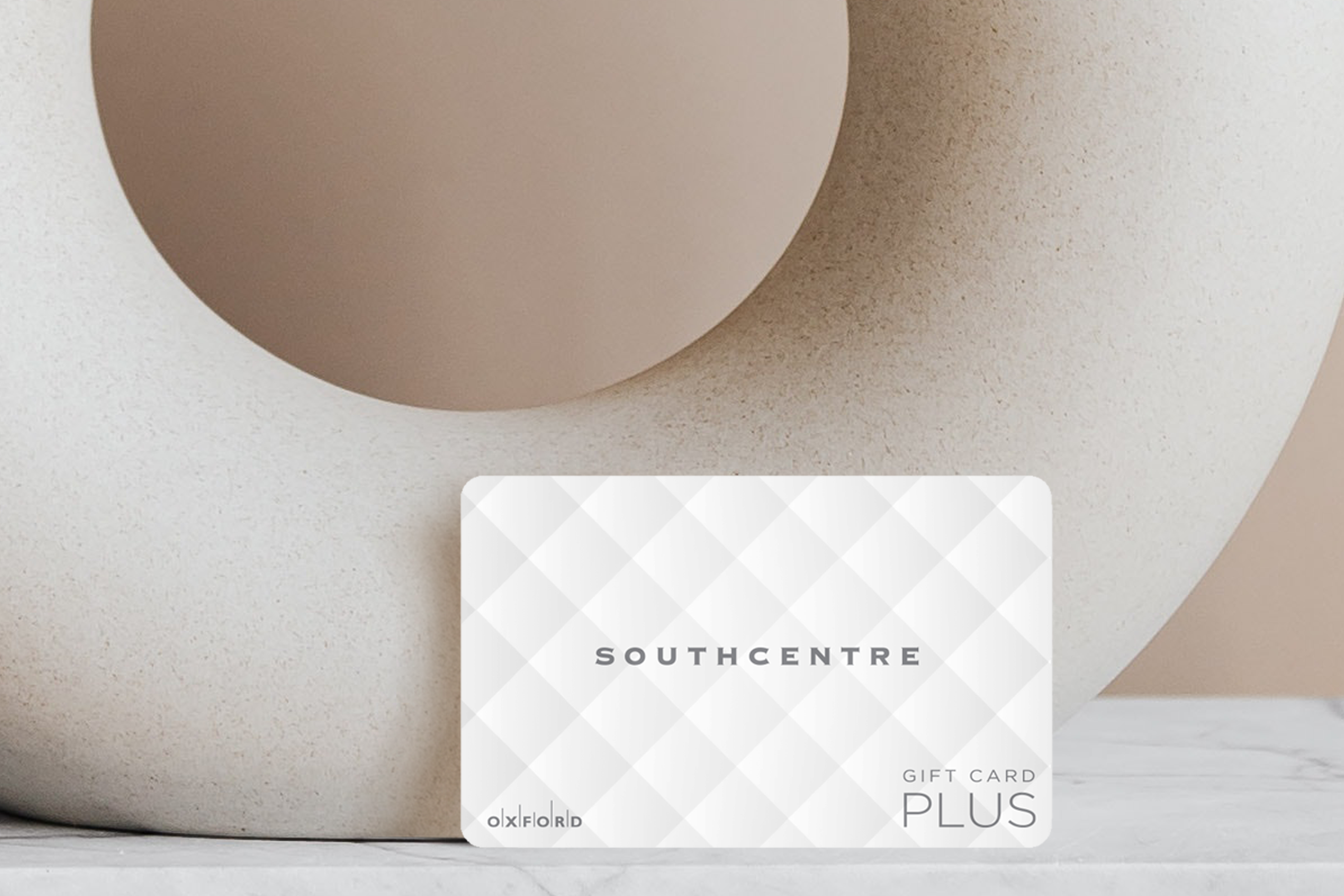 Southcentre white quilted gift card leaning against beige circular vase with a taupe wall.