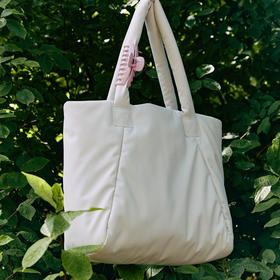 Cream coloured duffel bag with greenery in background